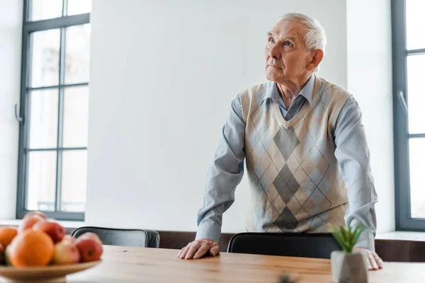 Trauriger älterer Mann, der während der Quarantäne mit Früchten am Tisch steht, selektiver Fokus — Stockfoto