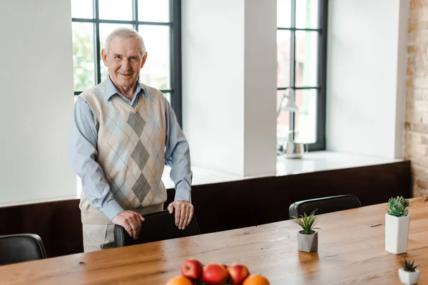 Glücklicher Senior, der während der Selbstisolierung mit Früchten und Pflanzen am Tisch steht — Stockfoto