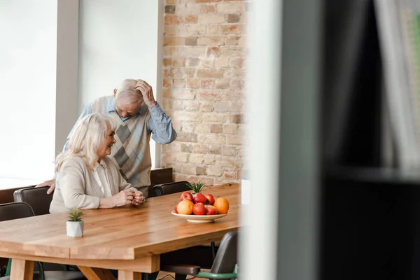 Happy elderly couple sitting at table with fruits during quarantine, selective focus — Stock Photo