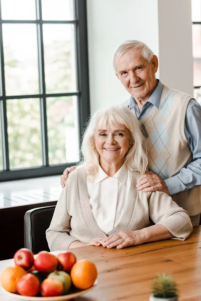 Sonriente pareja de ancianos sentados a la mesa con frutas - foto de stock
