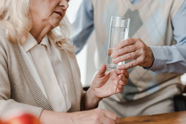 Vista cortada de marido idoso e esposa doente com copo de água em casa durante a quarentena — Fotografia de Stock