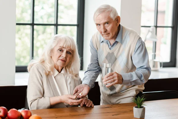 Тривожний літній чоловік і хвора дружина з таблетками і склянкою води вдома під час карантину — стокове фото