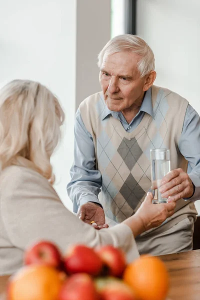 Worried senior husband and sick wife with pills and glass of water at home during quarantine — Stock Photo