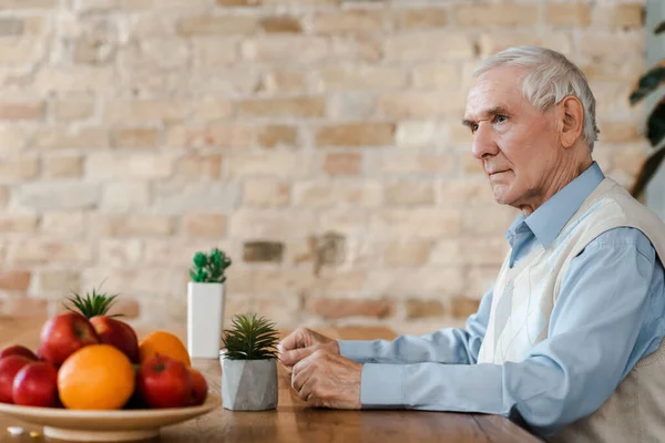 Hombre mayor solitario con frutas y plantas en la mesa durante el autoaislamiento - foto de stock
