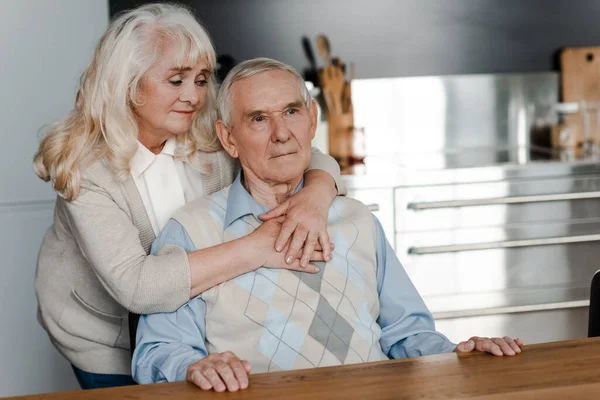 Triste anciano esposa y marido abrazando y sentado en casa en cuarentena - foto de stock