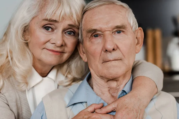 Расстроены старшая жена и муж обнимаются и сидят дома на карантине — стоковое фото