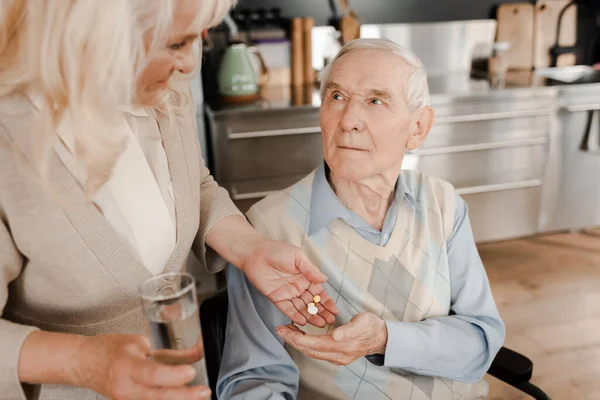 Elderly wife and sick husband with pills and glass of water at home during quarantine — Stock Photo