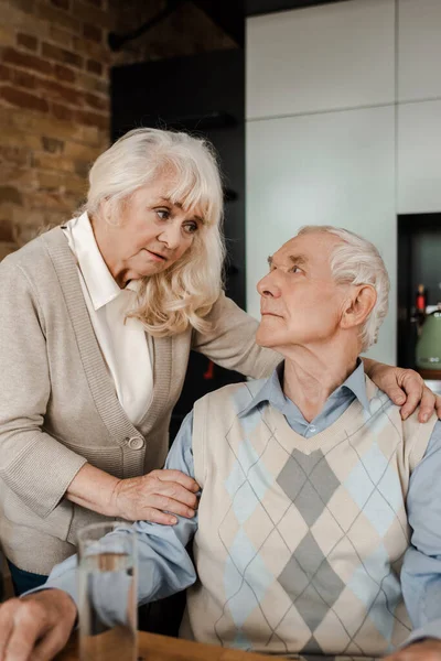Пожилая жена и больной муж со стаканом воды дома во время карантина — стоковое фото