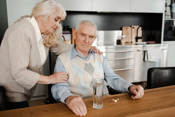 Esposa anciana y marido enfermo con pastillas y vaso de agua en casa en cuarentena - foto de stock