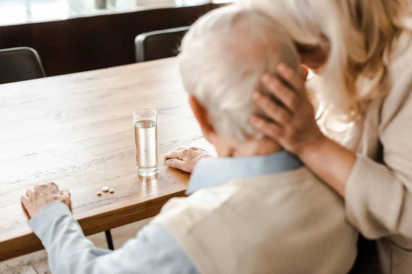 Moglie anziana e marito malato con pillole e bicchiere d'acqua a casa su auto isolamento, messa a fuoco selettiva — Foto stock