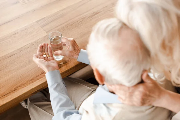 Sconvolto coppia di anziani malati con pillole e bicchiere d'acqua a casa su auto isolamento, messa a fuoco selettiva — Foto stock