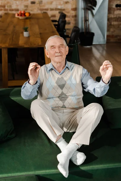 Feliz anciano meditando con los ojos cerrados en casa durante el autoaislamiento - foto de stock