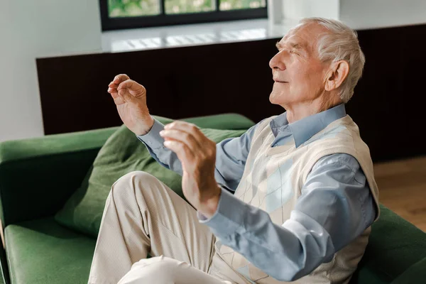 Positive senior man meditating with closed eyes on sofa during quarantine — Stock Photo