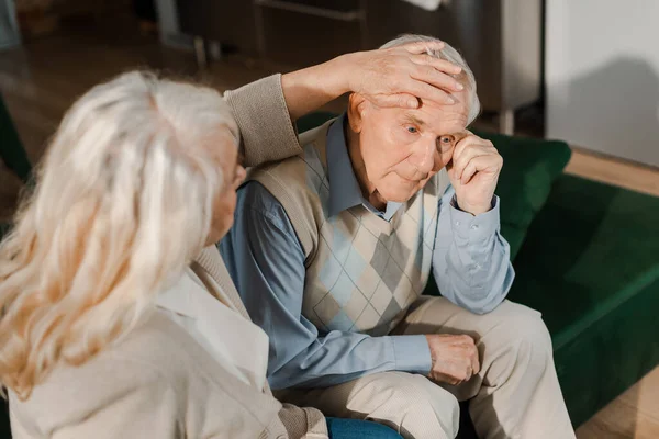 Беспокойная старшая жена проверяет температуру мужа дома на карантине — стоковое фото