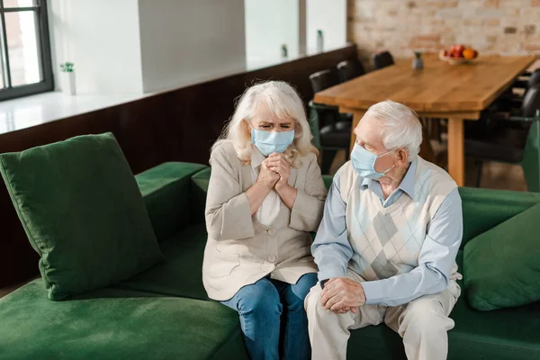 Esposa idosa doente e marido em máscaras médicas sentado no sofá durante a epidemia de coronavírus — Fotografia de Stock