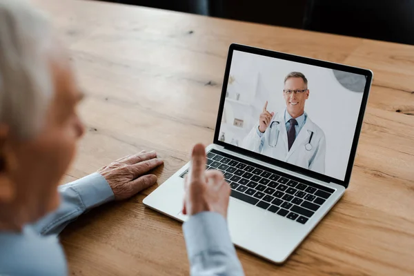 Vista recortada del anciano mostrando el pulgar hacia arriba y tener chat de vídeo con el médico masculino durante la cuarentena - foto de stock