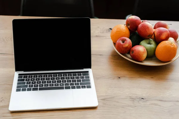 Portátil con pantalla en blanco de pie en la mesa de madera con frutas en casa - foto de stock
