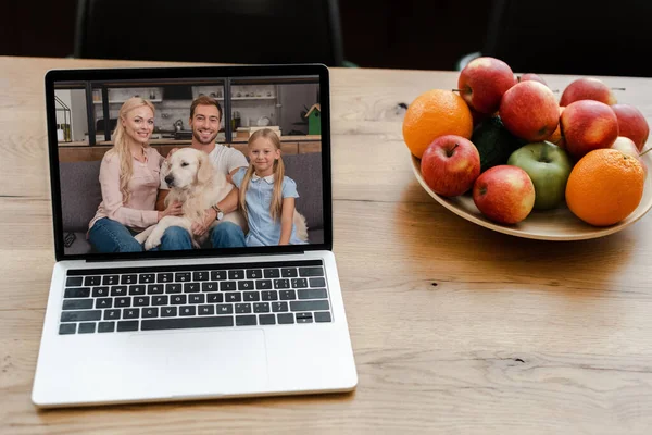 Primo piano di computer portatile con famiglia e cane sullo schermo sul tavolo con frutta — Foto stock