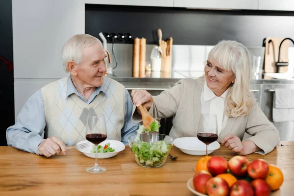 Feliz esposa sênior e marido jantar com vinho e salada em casa em quarentena — Fotografia de Stock