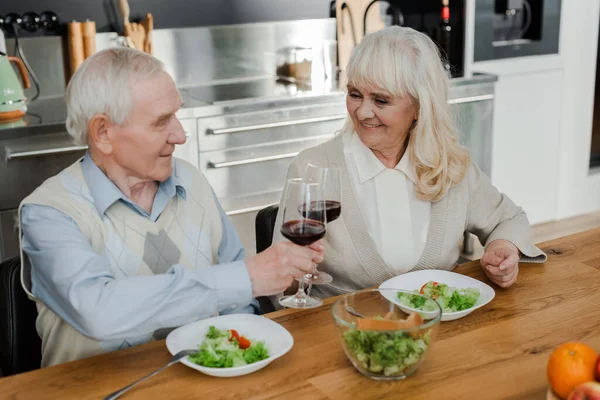 Glückliches Senior-Ehepaar beim Abendessen mit Wein und Salat zu Hause auf Selbstisolierung — Stockfoto