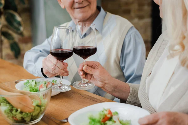 Vista recortada de pareja de ancianos cenando con vino y ensalada en casa en auto aislamiento - foto de stock