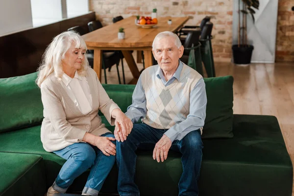 Upset elderly couple holding hands on sofa during self isolation — Stock Photo