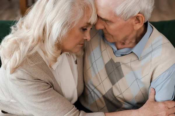 Triste pareja de ancianos abrazando y sentado en casa en cuarentena — Stock Photo