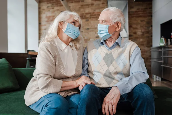 Sad elderly couple in medical masks sitting at home during self isolation — Stock Photo
