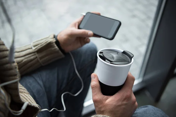 Человек держит термос чашку и смартфон — стоковое фото
