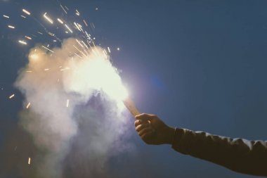 cropped view of male hand with smoke bomb with sparks at night clipart