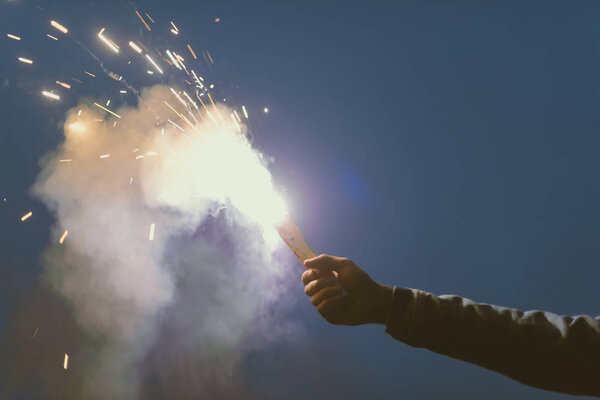 cropped view of male hand with smoke bomb with sparks at night