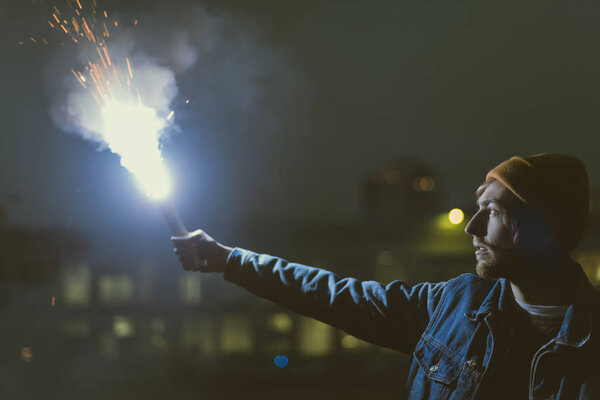 man holsing smoke bomb with sparks at night