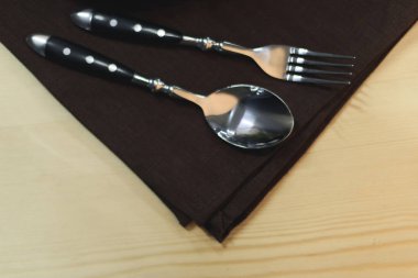 close up view of steel fork and spoon on napkin on wooden tabletop clipart