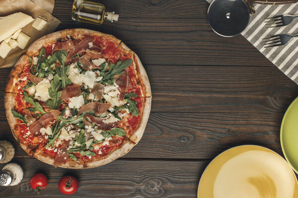 flat lay with arranged italian pizza, cutlery and various ingredients on wooden surface