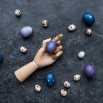 Mannequin hand with painted chicken and quail eggs on dark background
