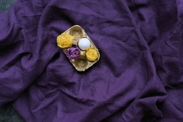 Куриное яйцо и цветы в коробке на текстильном фоне
