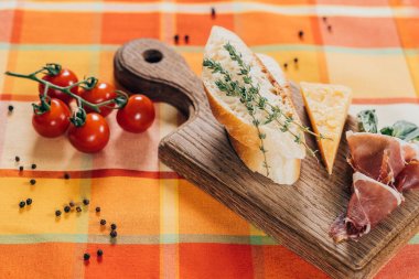 top view of sliced baguette, meat and parmesan cheese on wooden cutting board and fresh cherry tomatoes on table top clipart