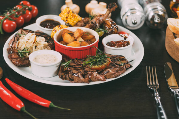 plate with sauces, roasted potatoes, grilled meat and vegetables on table 