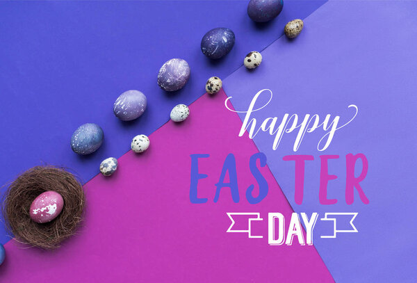 Ряды раскрашенных куриных и перепелиных яиц и гнездо с радостным пасхальным днем надписи на фоне в фиолетовых тонах
