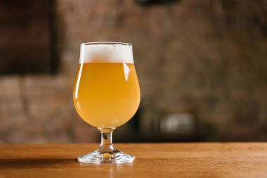 delicious fresh beer with foam in glass on wooden table in bar