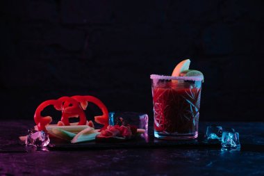 delicious bloody mary cocktail in glass and vegetables with melting ice cubes on dark surface  clipart