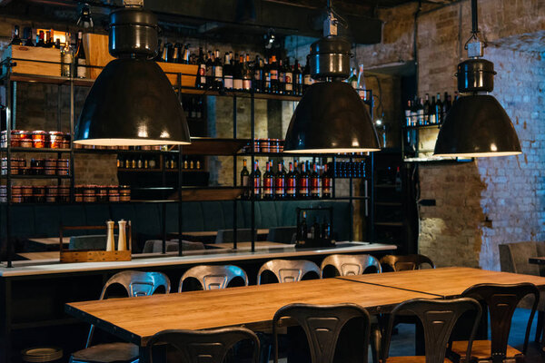 деревянные столы, лампы и барная стойка в современном ресторане
