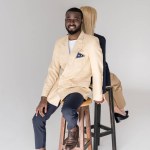 Élégant jeune couple multiethnique assis dos à dos, homme souriant à la caméra isolé sur gris