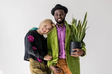 Interracial şık çift gri izole saksı poz içinde yeşil bitki ile gülümseyen portresi