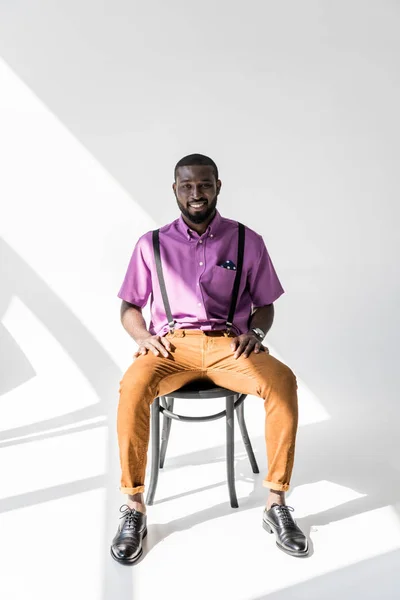 灰色の背景に椅子に座ってファッショナブルな衣料品のアフリカ系アメリカ人の笑顔 — ストック写真