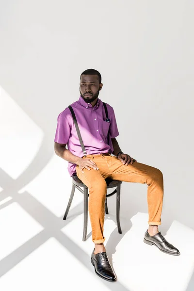 灰色の背景に椅子に座ってスタイリッシュな服で物思いにふけるのアフリカ系アメリカ人  — 無料ストックフォト