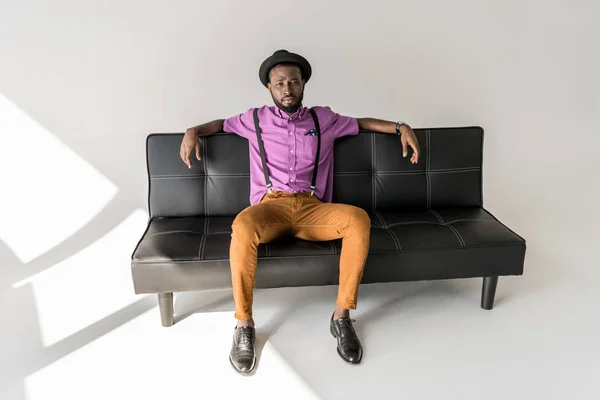 Thoughtful African American Fashionable Man Resting Black Sofa Grey Background — Stock Photo, Image