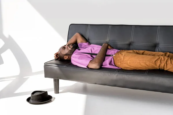 Афроамериканський Модний Чоловік Лежить Чорному Дивані Капелюхом Підлозі Сірому Фоні — стокове фото