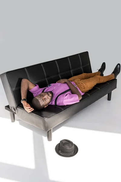 African American Fashionable Man Lying Black Sofa Hat Floor Grey — Foto Stok Gratis