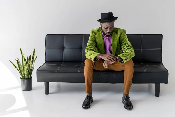 Африканский Модный Мужчина Шляпе Проверяет Время Сидя Черном Диване — Бесплатное стоковое фото